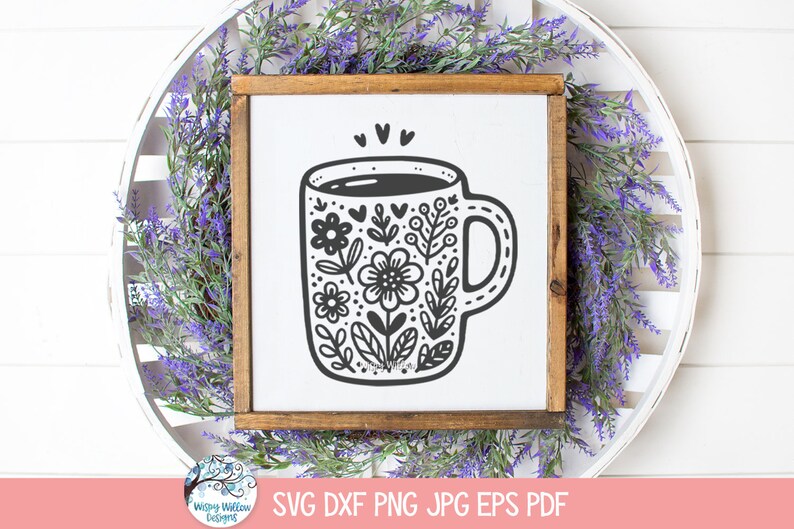 Op de afbeelding: Een zwart-witte illustratie van een koffiemok met een bloemenontwerp. De mok is gevuld met koffie en heeft een hart erboven.