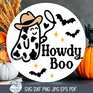 May include: A white circle with a black and white ghost wearing a cowboy hat and the text "Howdy Boo". The ghost is holding a lasso with hearts on it. There are also black bats and yellow stars around the ghost.