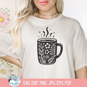 May include: A white t-shirt with a black and white illustration of a coffee mug with floral designs. The mug has steam coming from it and the text "Whispy Willow" is at the bottom of the mug.