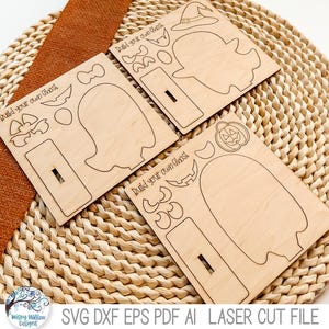 May include: Three light-colored wooden sheets featuring laser-cut outlines for a build your own ghost project. Each sheet includes a ghost shape, a rectangular base with a slot, and various accessories like hats, pumpkins, and facial features.