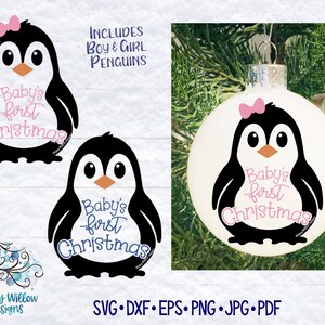 May include: A Christmas ornament featuring a black and white penguin design with a pink bow. The text "Baby's first Christmas" is written in pink script. The image also includes a penguin design with blue text and the words "Includes Boy & Girl Penguins".