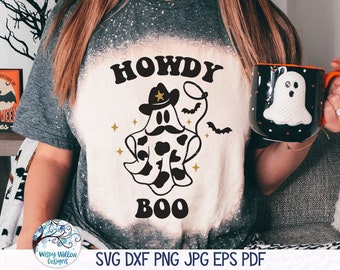 May include: A charcoal grey bleached t-shirt featuring a graphic of a ghost wearing a cowboy hat and mustache with cow print patterns. The text HOWDY BOO is printed in black above and below the ghost, accompanied by small gold stars and bats.