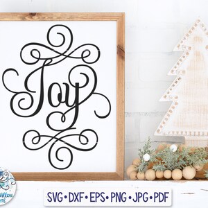 Puede incluir: Un letrero blanco con la palabra "Alegría" escrita en cursiva negra y rodeada de remolinos decorativos. El letrero está enmarcado en madera y está sentado en un estante blanco con un árbol de Navidad de madera y una guirnalda de cuentas de madera.