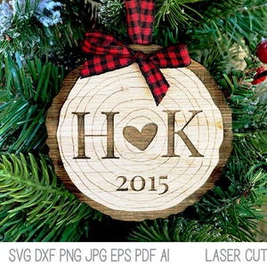 Op de afbeelding: Een houten kerstversiering in de vorm van een boomstam met de initialen "HOK" en het jaar "2015" erop gegraveerd. Een rood-zwart geruit lint is om de versiering gebonden.