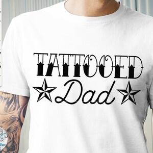 May include: A white t-shirt featuring the black text TATTOOED Dad with a star on each side of the word Dad. The text SVG, DXF, EPS, PNG, JPG, PDF is visible on the left side. The design is printed on the front of the shirt.