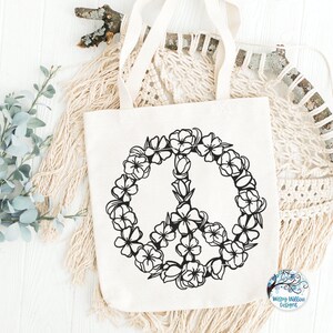 May include: A white tote bag with a black peace sign made of flowers. The peace sign is surrounded by a wreath of flowers.
