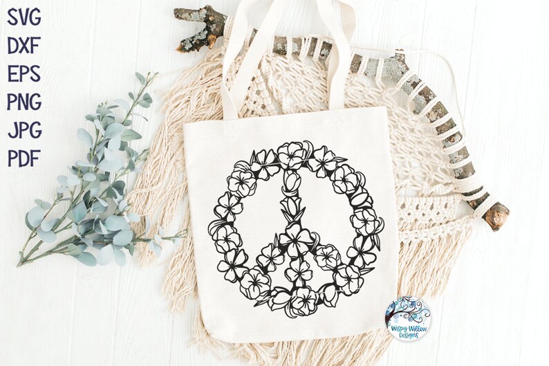 May include: A white tote bag with a black peace sign made of flowers. The peace sign is surrounded by a wreath of flowers.