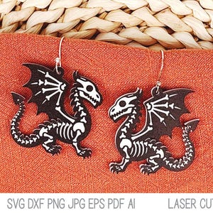 Könnte beinhalten: Ein Paar Ohrhänger mit einer schwarzen Drachensilhouette und einem weißen Skelett-Design auf der Oberfläche. Die Ohrringe sind an silberfarbenen Metallhaken befestigt und zeigen eine detaillierte, lasergeschnittene Drachenform.