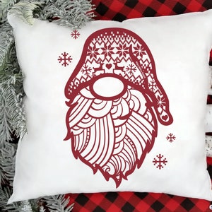 May include: Red and white patterned gnome head with a beard and a snowflake design. The gnome is on a white pillow with a red and black plaid background.