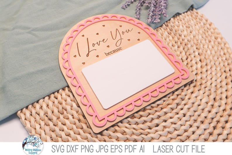 May include: An arched wooden sign with a pink scalloped border and the text "I Love You because" engraved in black. The sign features a large, blank white rectangular space for writing and small engraved heart accents on the light wood surface.