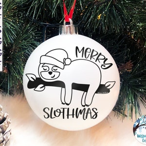 May include: A white spherical Christmas ornament featuring a black graphic of a sloth wearing a Santa hat while resting on a branch. The text MERRY SLOTHMAS is printed in black. The ornament has a silver cap and a red ribbon for hanging.