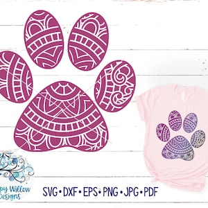 May include: A purple paw print with a mandala design. The paw print is on a white wooden background. The image also includes a pink t-shirt with the same paw print design in a gradient of purple and blue.