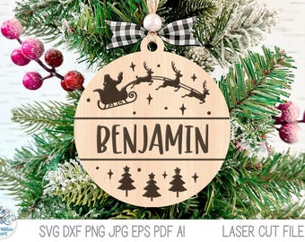 May include: A round wooden Christmas ornament featuring a laser-cut design of Santa in a sleigh pulled by reindeer above the name BENJAMIN, with three pine trees at the bottom, accented by a white bead and a black and white buffalo plaid ribbon.