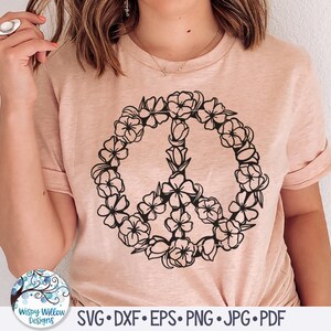 May include: A pink t-shirt with a black peace sign design made of flowers. The peace sign is surrounded by a circle of flowers.