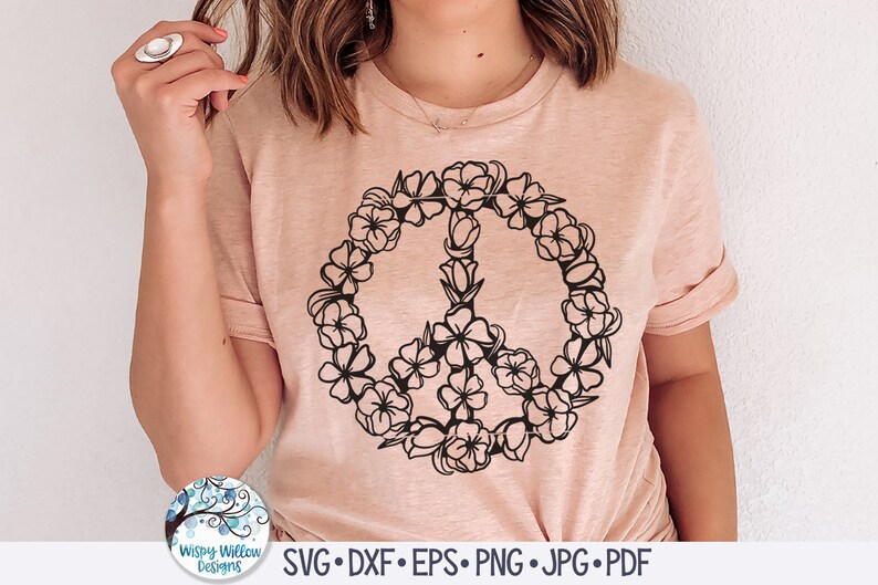 May include: A pink t-shirt with a black peace sign design made of flowers. The peace sign is surrounded by a circle of flowers.