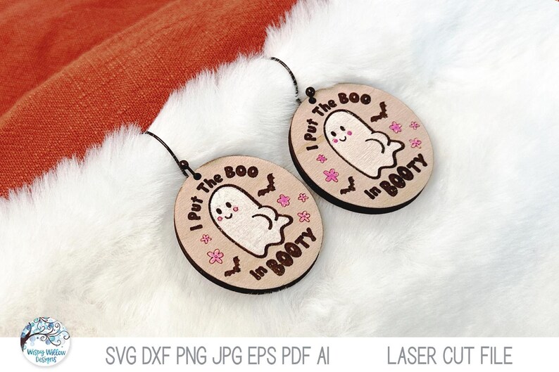 May include: A pair of round, light-colored wooden earrings featuring a laser-engraved cartoon ghost, small bats, and pink flowers. The text I Put The Boo In BOOTY is printed in black around the ghost. Each earring has a black metal hook.
