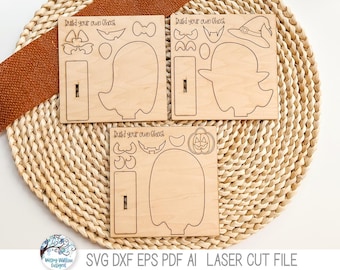 May include: Three wooden laser cutouts with the text "Build your own ghost". Each cutout features a ghost shape and various accessories like hats, bows, and pumpkin faces. The cutouts are on a woven mat with a brown fabric accent.