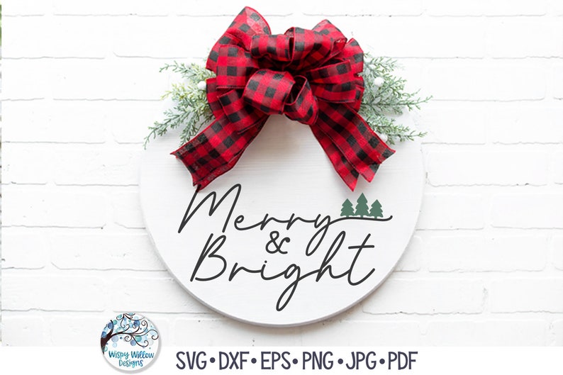 May include: A round white wooden sign featuring the black text Merry & Bright with three small green pine trees. A large red and black buffalo plaid ribbon bow is attached to the top, accented with green pine sprigs and small white berries.