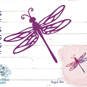 May include: Purple dragonfly silhouette design, perfect for crafting projects like iron-on transfers, vinyl decals, or stencils.  The design is shown on a white wood background with a pink t-shirt mockup.