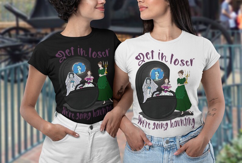 May include: Black and white t-shirts with the text "Get in loser, We're going haunting." The shirts feature a cartoon graphic of a haunted carriage with three women. One shirt is black, the other is white.