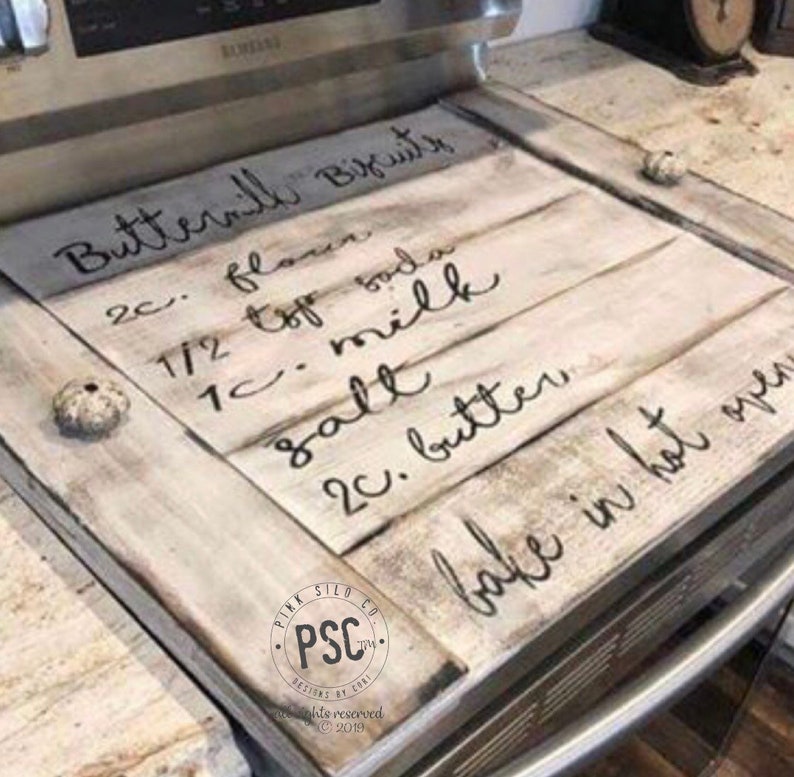 Może przedstawiać: Biały drewniany znak z czarnym ręcznie pisanym tekstem, kt&oacute;ry brzmi "Buttermilk Biscuits 2c. mąki 1/2 łyżeczki sody 1c. mleka 1/2 soli 2c. masła Piec w gorącym piekarniku" z małym logo w lewym dolnym rogu, kt&oacute;re brzmi "Pink Silo Co. PSC Designs by Cort Wszelkie prawa zastrzeżone &copy; 2019"
