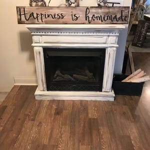 May include: A white painted fireplace mantel with a wooden sign above it that reads "Happiness is homemade".