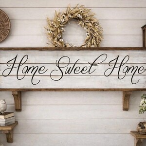 May include: A rustic farmhouse-style wall decor arrangement. A wooden sign with "Home Sweet Home" in elegant script is the focal point. The scene includes a woven wreath, a lantern, and floral arrangements, creating a cozy, inviting atmosphere.