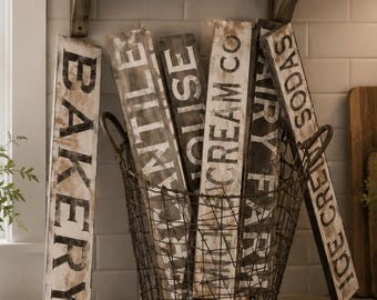 May include: A rustic kitchen scene with wooden signs in a wire basket. Signs read "Bakery", "Antiques", "Cream Co", "Dairy Farm", and "Ice Cream Sodas". A sign above says "Homemade Happiness is Made Here".