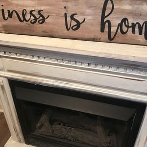 May include: A white painted fireplace mantel with a black metal fireplace insert. A wooden sign above the mantel reads "Happiness is home".
