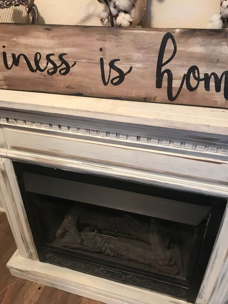 May include: A white painted fireplace mantel with a black metal fireplace insert. A wooden sign above the mantel reads "Happiness is home".
