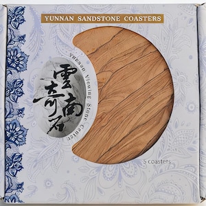 May include: A box of Yunnan Sandstone Coasters. The box is white with a paisley design and the text "Yunnan Sandstone Coasters". The coasters are a light brown color and have a unique texture. The box contains 5 coasters.