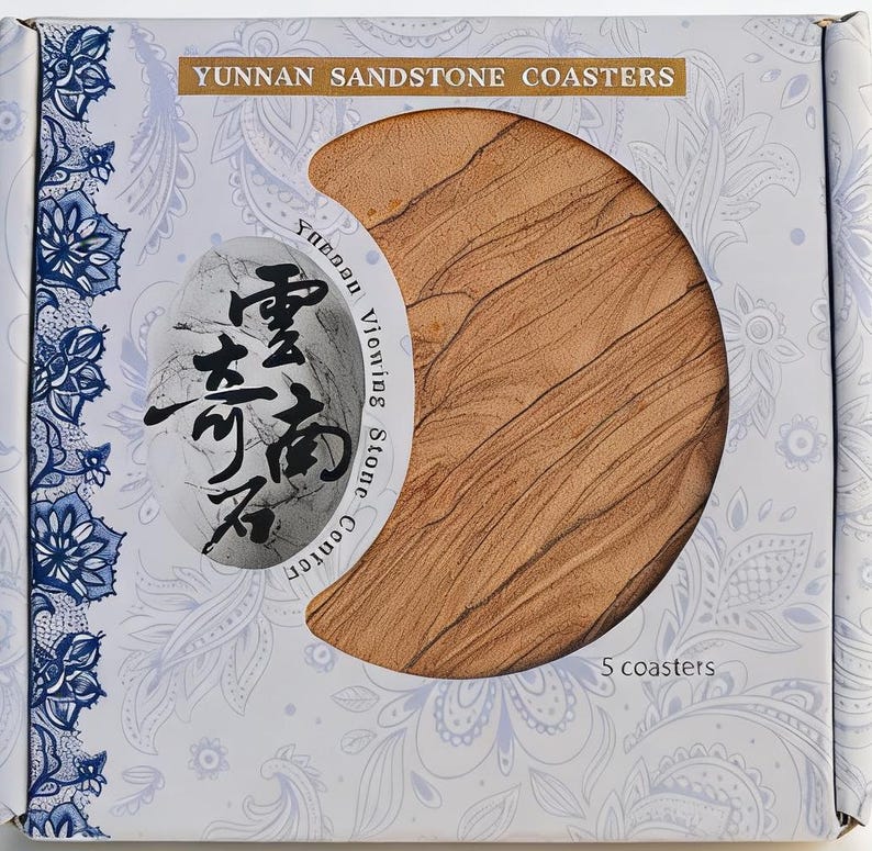 May include: A box of Yunnan Sandstone Coasters. The box is white with a paisley design and the text "Yunnan Sandstone Coasters". The coasters are a light brown color and have a unique texture. The box contains 5 coasters.