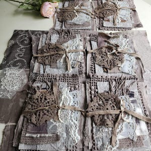 Pode incluir: Uma coleção de pacotes de tecido em camadas em tons de taupe, bege e creme. Cada pacote apresenta um centro de crochê marrom amarrado com uma fita bege, sobreposto a várias texturas, incluindo renda e tecido bordado.
