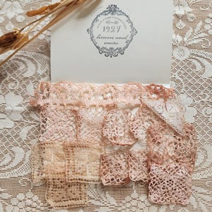 May include: A collection of small, square, and circular lace doilies in varying shades of soft pink and cream. The lace pieces are arranged on a white card featuring a circular logo with the text 1924 linens and more, placed against a white lace fabric background.
