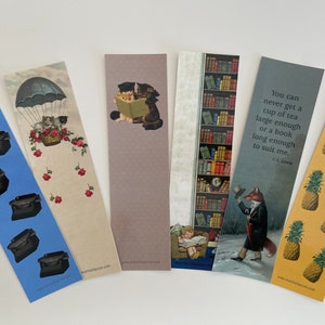 May include: Set of six colourful bookmarks featuring various illustrations and quotes. One bookmark has a blue background with black typewriters, another has a hot air balloon with kittens, another has two cats reading a book, another has a bookshelf filled with books, another has a fox in a top hat and another has a yellow background with pineapples. The quote on one bookmark reads "You can never get a cup of tea large enough or a book long enough to suit me. C.S. Lewis."