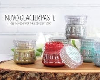 May include: Six jars of Nuvo Glacier Paste in various colors, including gold, red, teal, and silver. The jars are arranged in a pyramid shape on a wooden surface. The text "Nuvo Glacier Paste" is printed on the label of each jar.
