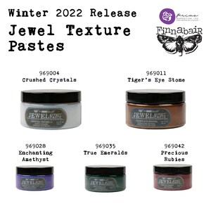 Op de afbeelding: Winter 2022 release van Jewel Texture Pastes van Finnabair. Vier potten met textuurverf in verschillende kleuren: gebroken kristallen, tijgeroog, betoverende amethist en echte smaragden. Elke pot is gelabeld met de productnaam en een uniek productnummer.