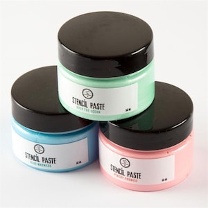 May include: Three pots of stencil paste with black lids. The pots are stacked, showing labels with the text "STENCIL PASTE" and colour names: "Over the Ocean", "Blue Madness", and "Peachy Promise". Each pot contains 50 ml of paste.