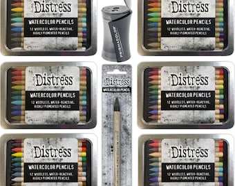 May include: Set of 12 watercolor pencils in a tin box with a sharpener. The pencils are woodless, water-reactive, and highly pigmented. The tin box is silver with black lettering and a distressed look. The pencils are arranged in a rainbow pattern.