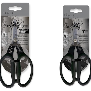 Può includere: Due forbici in titanio nere per mancini, lunghe 17,78 cm, con lame micro-seghettate, esposte su confezione grigia. La confezione presenta il marchio "Jim Holtz" e la parola "LEFTY" sulle forbici.