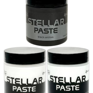 Op de afbeelding: Drie potten Stellar Paste met zwarte deksels. Eén pot is zwart met de tekst "black widow", en twee zijn wit met de teksten "crystal clear" en "white lie". Elke pot is gelabeld met de productnaam.