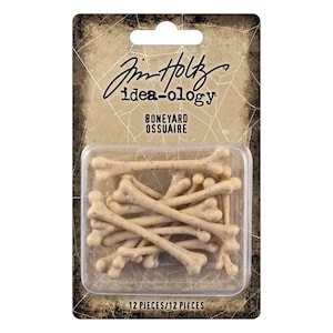 Peut inclure: Un paquet de 12 petites décorations en forme d'os de couleur beige. L'emballage porte la mention "Jim Holtz idea-ology BONEYARD OSSUAIRE" et le texte "12 PIECES/12 PIÈCES". Les os sont dans un contenant en plastique transparent.