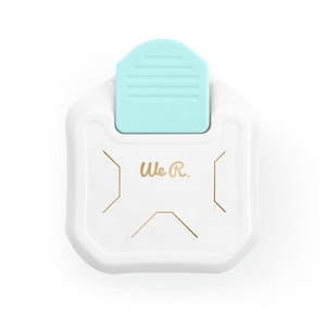 Puede incluir: Troquel de papel blanco con un mango azul claro. El troquel tiene forma de diseño geométrico con líneas doradas. El texto "We R." está impreso en el troquel.