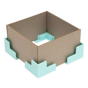 以下が含まれることがあります： 薄い青色のプラスチック製の角保護具が4つ付いた段ボール箱。箱は空で、保護具は角に取り付けられています。