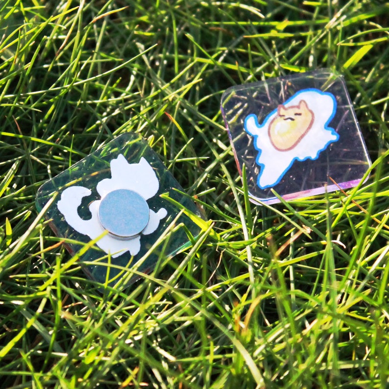 Two magnets lying in grass, the other one is back side up to show the magnet attached to it.