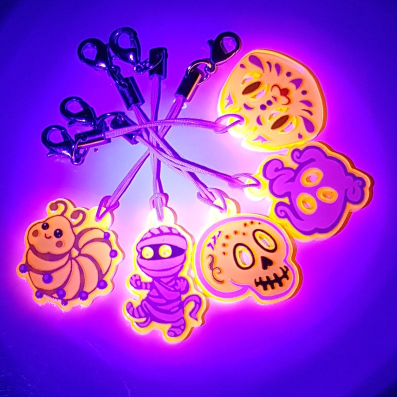 The same five charms as previous image but in UV light sho they appear to glow abd the white ink is showing up as purple. They are surrounded by pinkish purplish aura.
