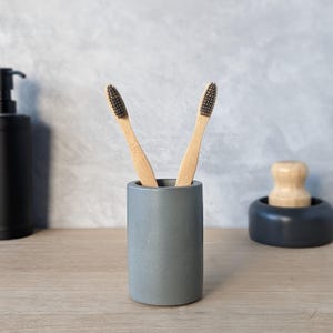 May include: A gray concrete toothbrush holder with two bamboo toothbrushes with black bristles.