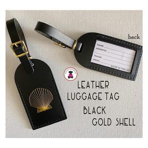 May include: Two black leather luggage tags with gold hardware. One tag features a gold seashell design, the other has a clear window for contact information. The text "Leather Luggage Tag Black Gold Shell" is visible.
