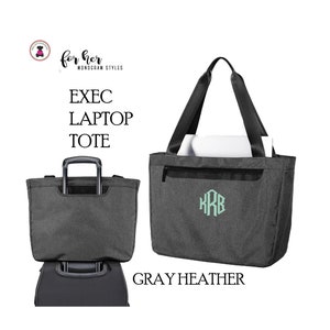May include: Gray heather tote bag with black straps and a zippered pocket. The bag has a monogrammed "KRB" in light green. The text "EXEC LAPTOP TOTE" is printed on the bag. The bag is shown on a suitcase.