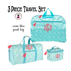 May include: A three-piece travel set in ocean blue with a white Greek key pattern. The set includes a garment bag, a duffel bag, and a cosmetic bag, each with a coral monogram and tassel accents. The text "3 PIECE TRAVEL SET" is at the top.